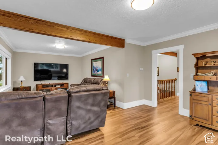 Spacious living area featuring wood-finish flooring, a prominent exposed wood beam, crown molding, and recessed lighting