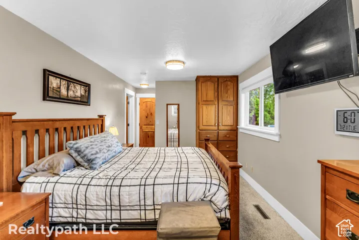 Bedroom featuring carpet flooring, built-in wooden cabinetry, a wall-mounted television, and a window with white trim