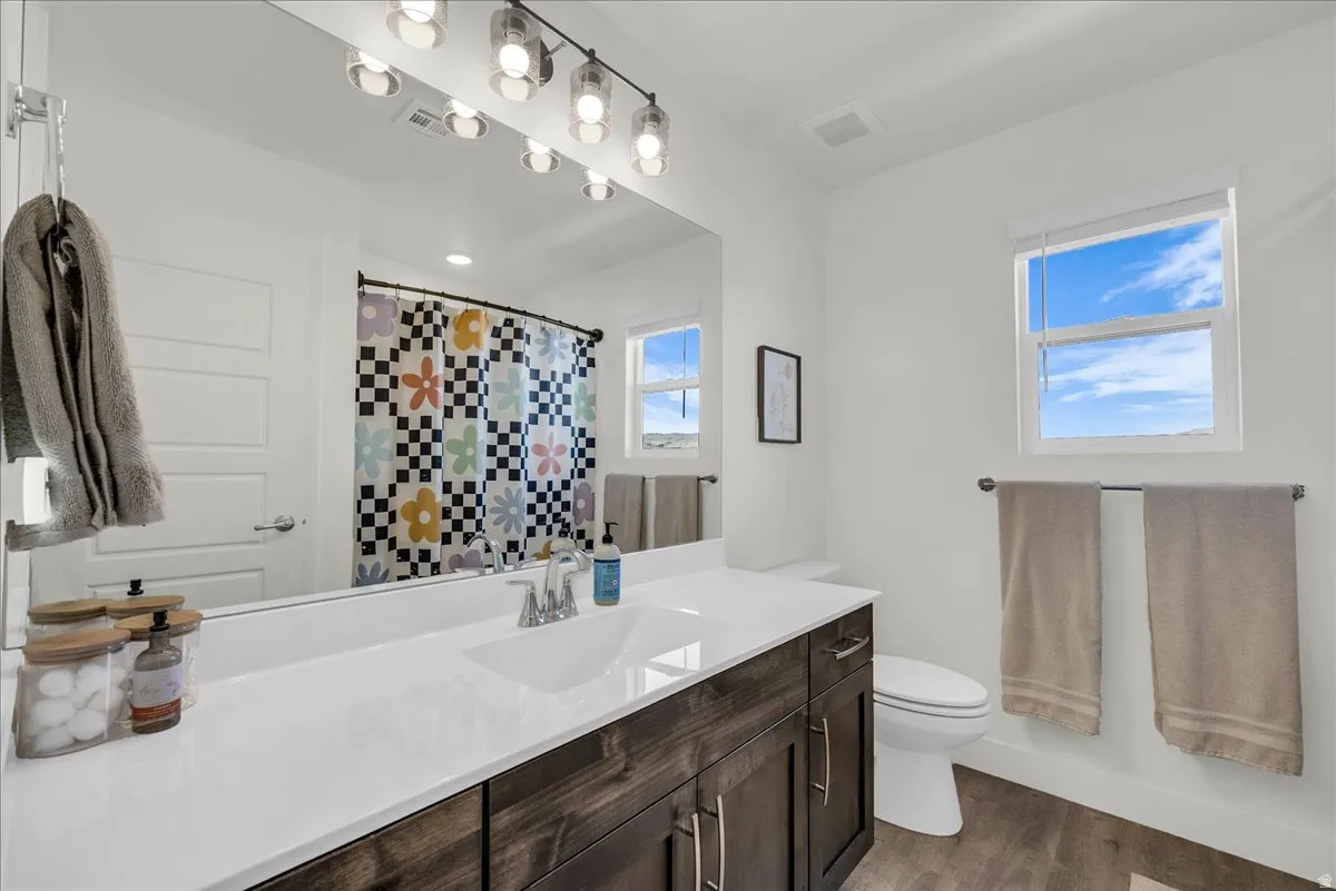 Bathroom featuring a wood-finish vanity with a white countertop and integrated sink, a large mirror, and track lighting