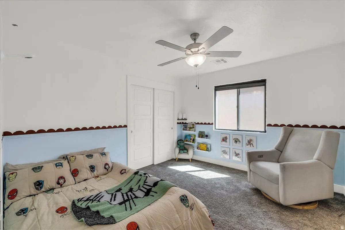 Carpeted room featuring a ceiling fan with integrated lighting, a window with a roller shade, and built-in shelving