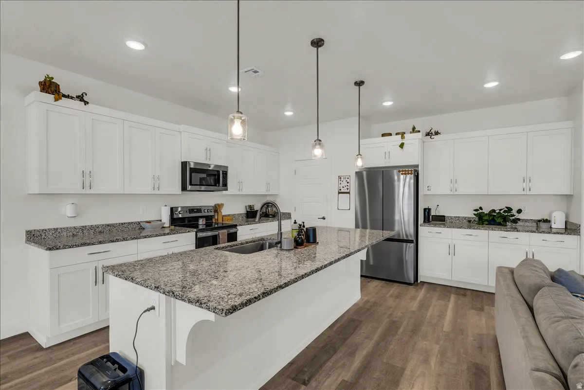 Kitchen featuring an extended island with a stainless steel sink, granite countertops, white shaker cabinetry, and wood-finish flooring