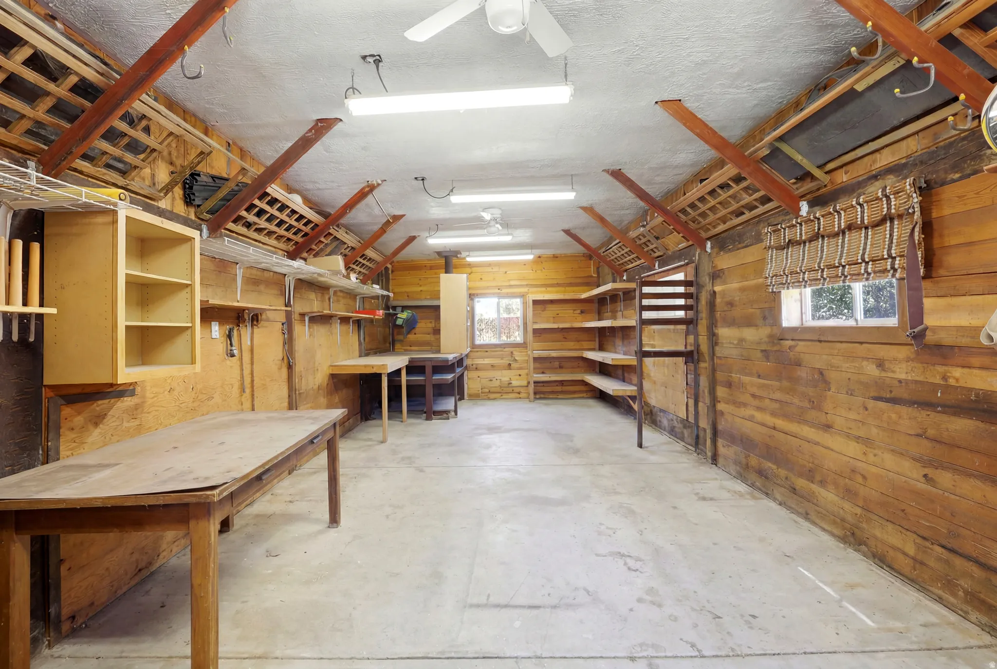 Spacious workroom featuring concrete flooring, exposed wood beam ceiling, and extensive built-in shelving