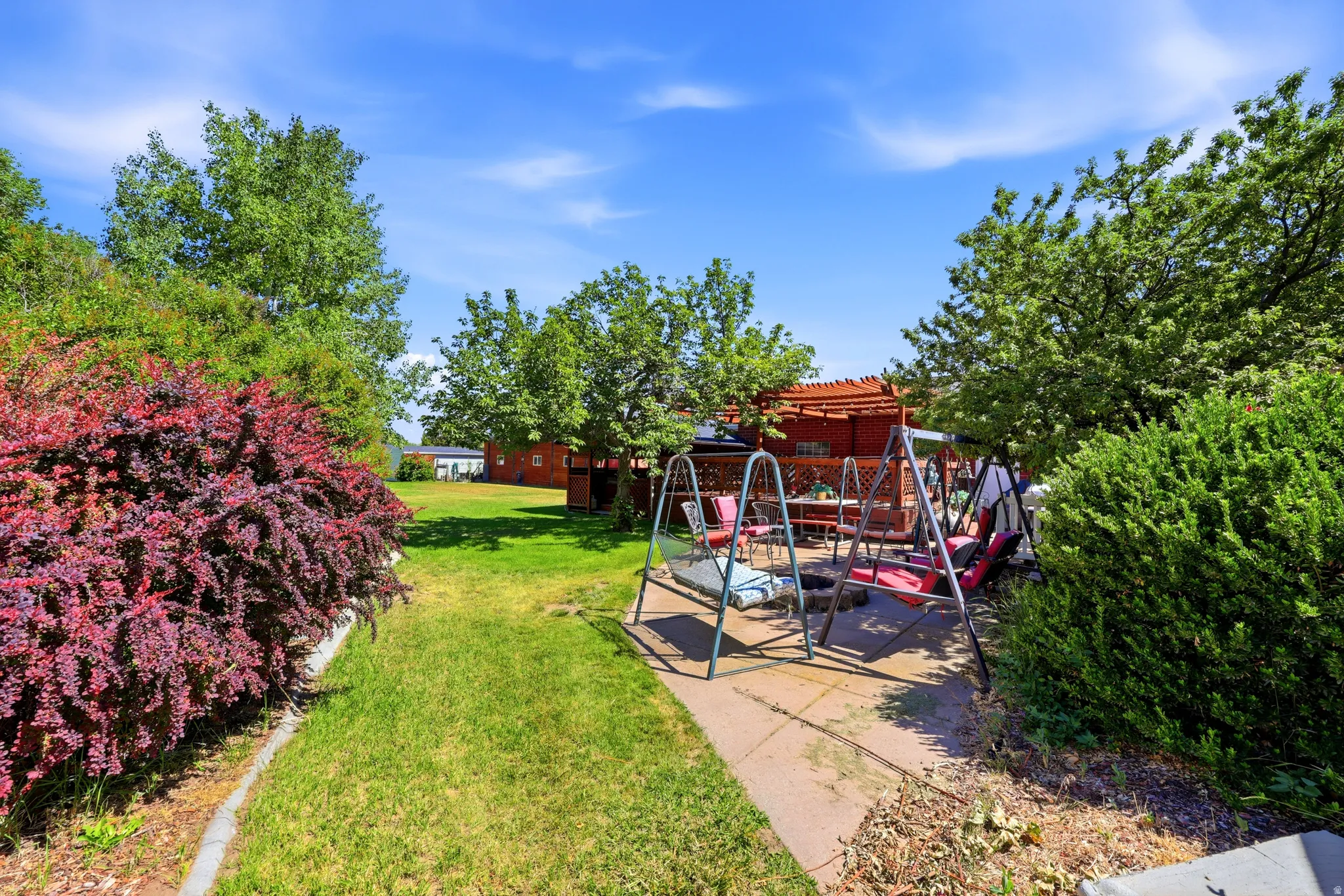Expansive green lawn with mature trees and vibrant red and green bushes
