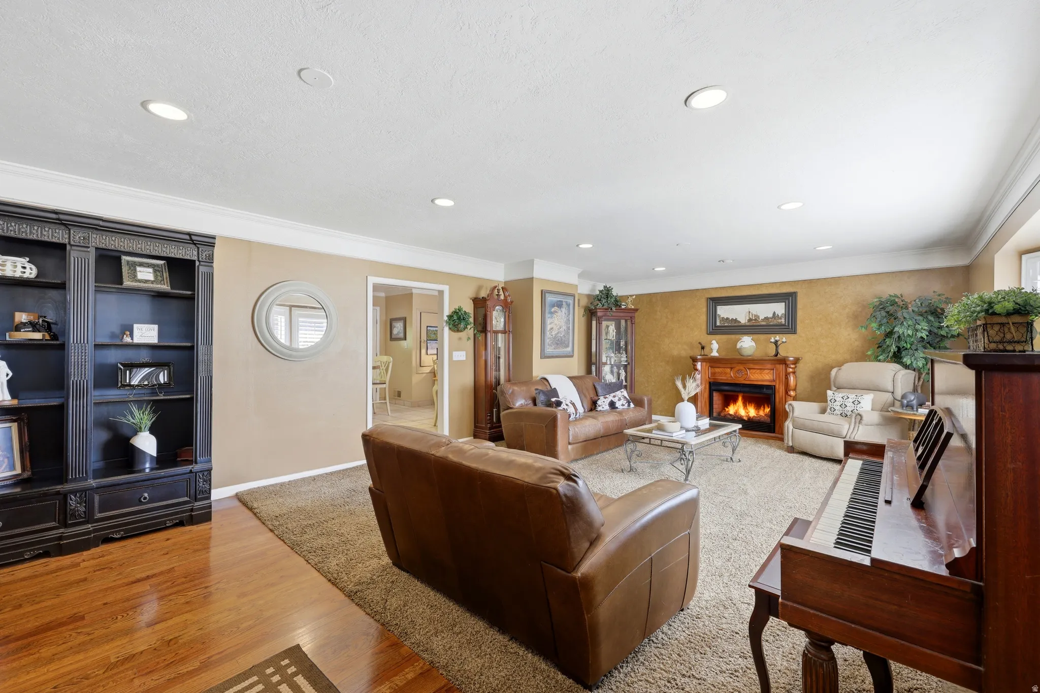 Spacious living area featuring a traditional fireplace with a carved wood mantel, recessed lighting, crown molding, and a built-in dark wood bookcase