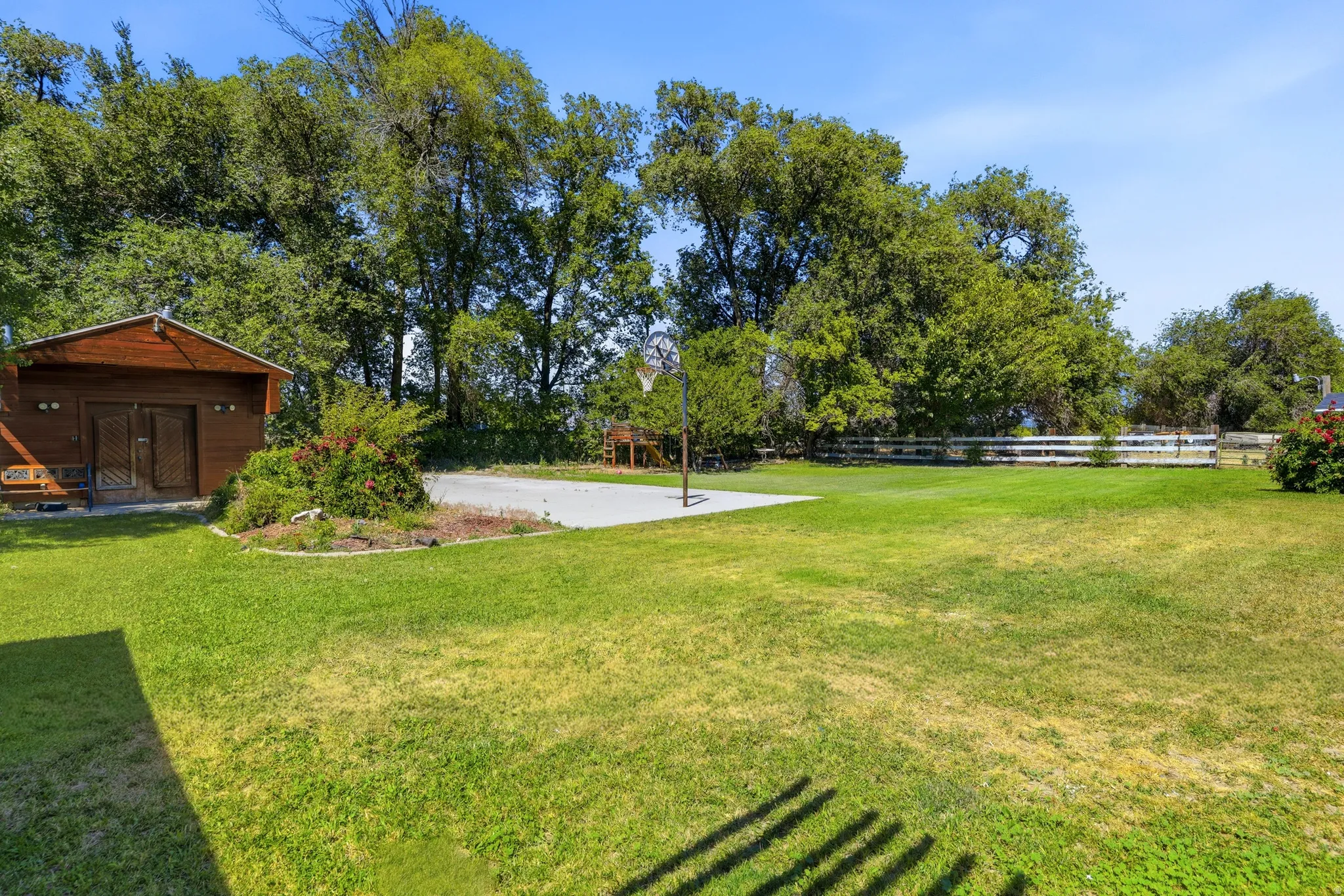 Expansive grassy yard featuring a concrete pad, basketball hoop, and a wood-sided outbuilding with double doors