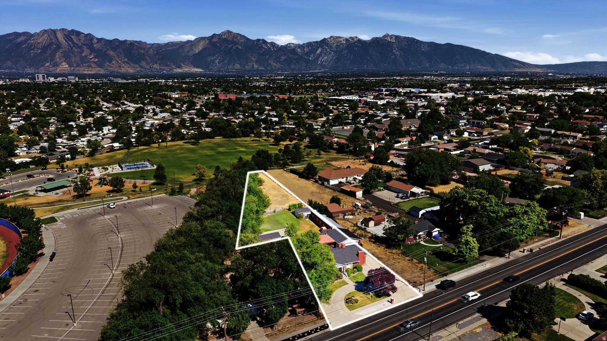 Expansive property featuring a paved driveway, mature trees, and a mountain backdrop