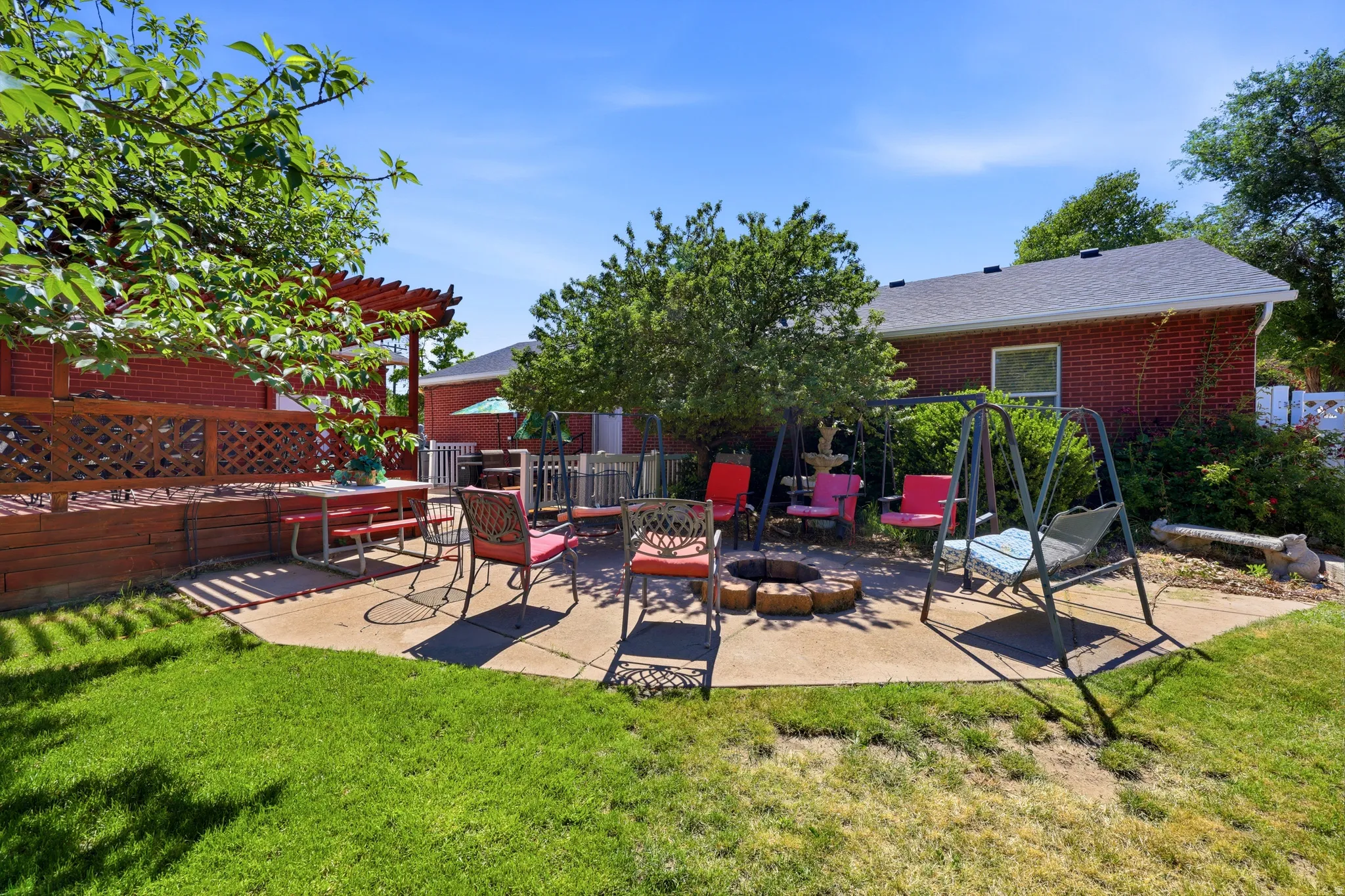 Expansive concrete patio area with a fire pit feature, surrounded by mature trees and manicured lawn