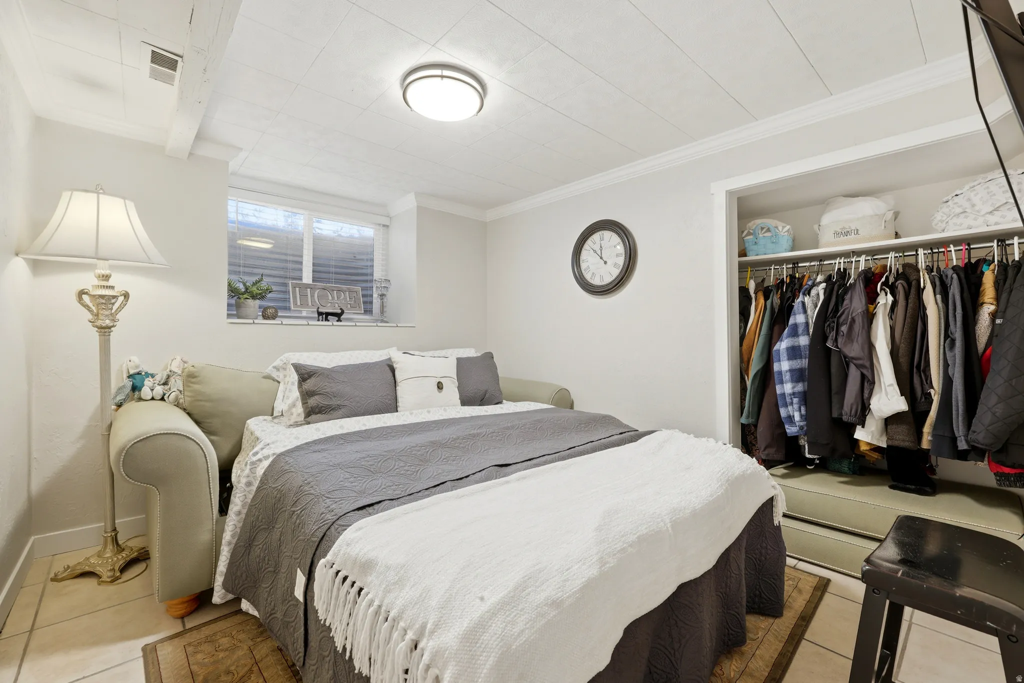 Recessed window with blinds, white paneled ceiling, overhead flush-mount lighting, and built-in closet with shelving and hanging rod