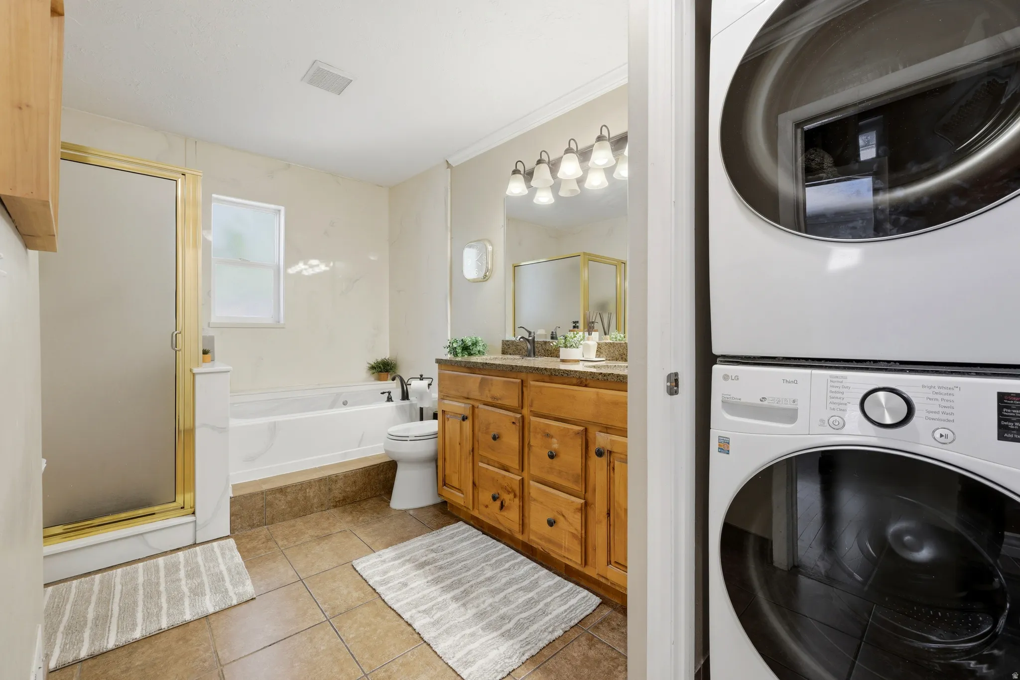 Bathroom featuring a gold-framed shower enclosure, a built-in jetted tub, a wood vanity with a stone-finish countertop, and tile flooring