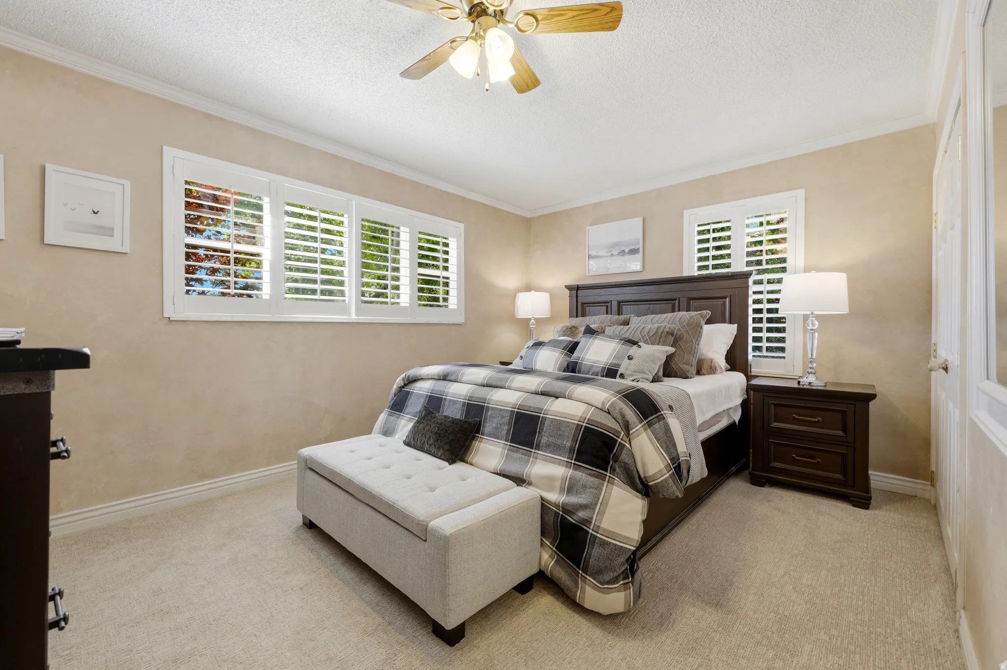 Bedroom featuring two windows with white plantation shutters, crown molding, and a ceiling fan