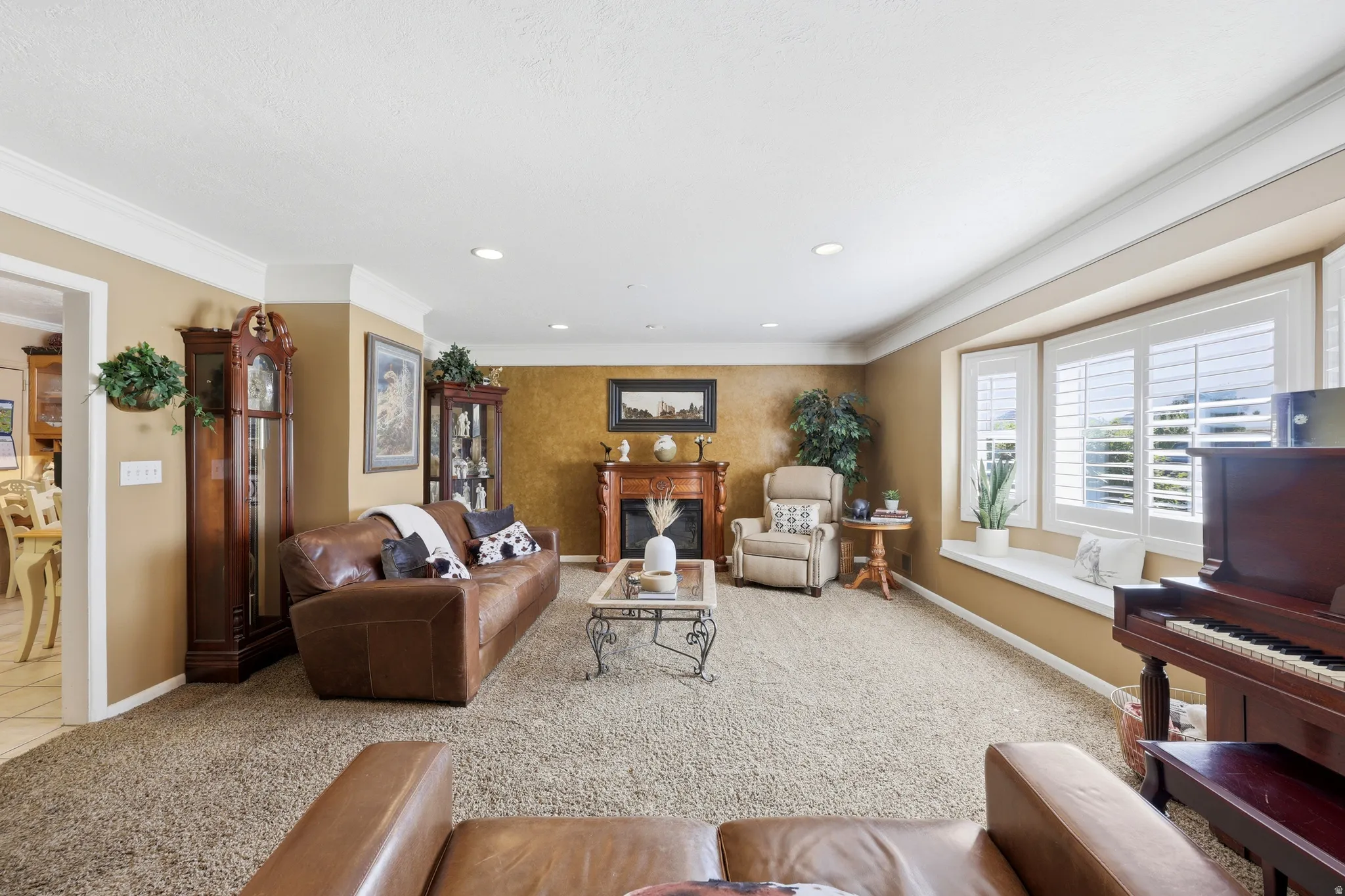 Carpeted living area featuring a fireplace with wood mantel, bay window with plantation shutters, recessed lighting, and crown molding