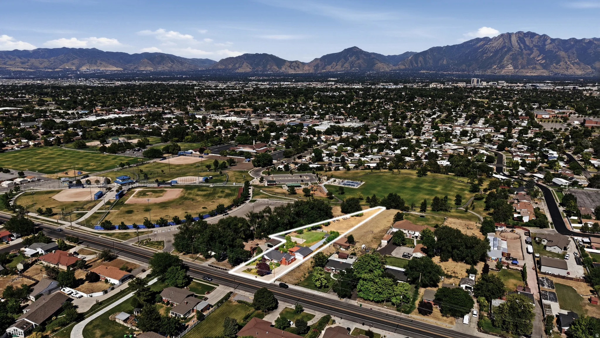 Aerial perspective showcasing a residential property with a defined lot, situated across from a park with baseball fields and green spaces