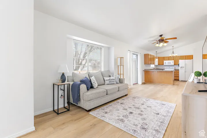 Bright open-concept living space featuring wood-finish flooring, white walls, and a large window with blinds