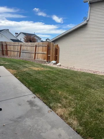 Concrete patio leading to a grassy area, bordered by a wood fence, and the property exterior featuring horizontal siding