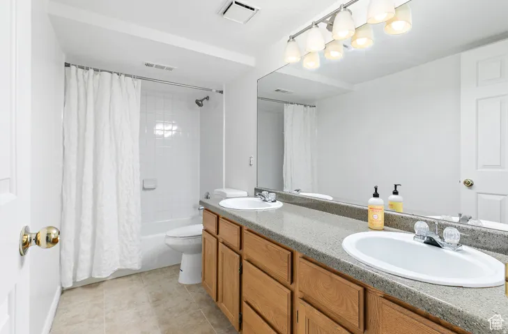 Bathroom featuring a double vanity with light wood cabinetry and a speckled countertop