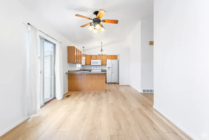Open-concept living area with light wood-finish flooring, vaulted ceilings, and a ceiling fan with integrated lighting