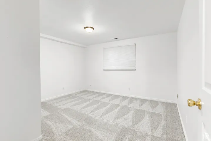 Carpeted room with a window featuring a white roller shade, white walls, and a ceiling-mounted light fixture