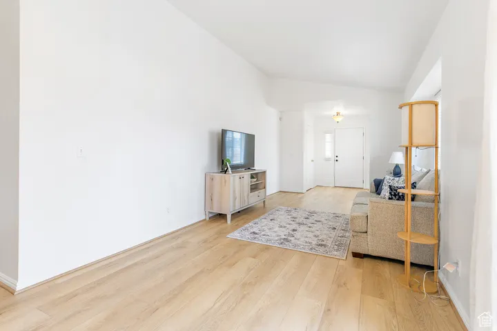 Living area featuring wood-finish flooring, vaulted ceilings, and a front entry door with a sidelight