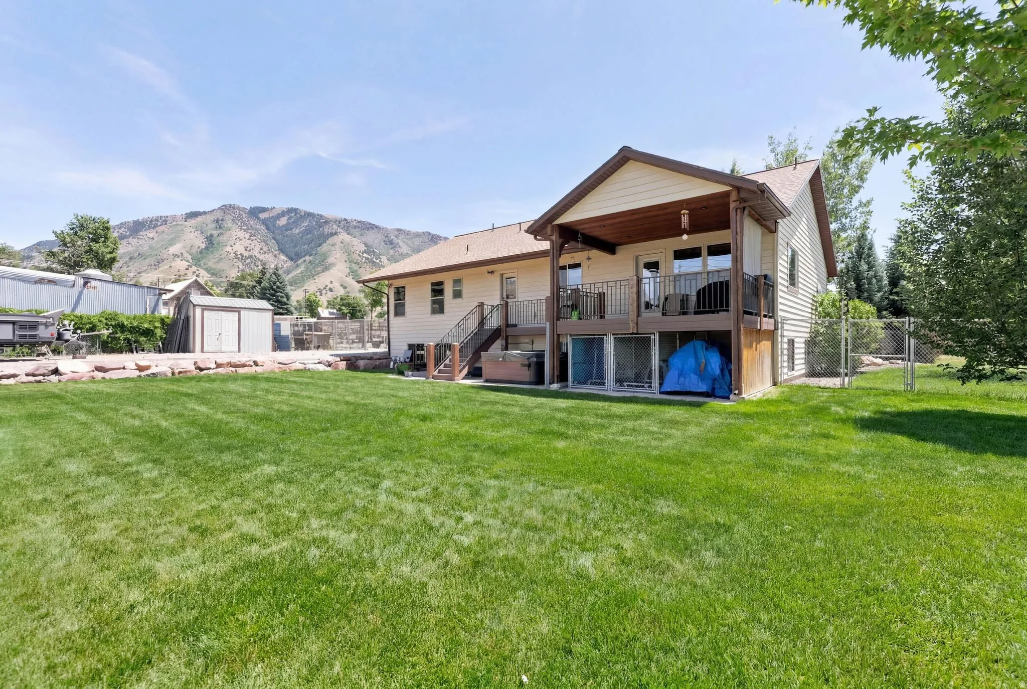 Expansive green lawn with a two-story home featuring a covered upper-level deck and a lower-level patio with sliding glass doors