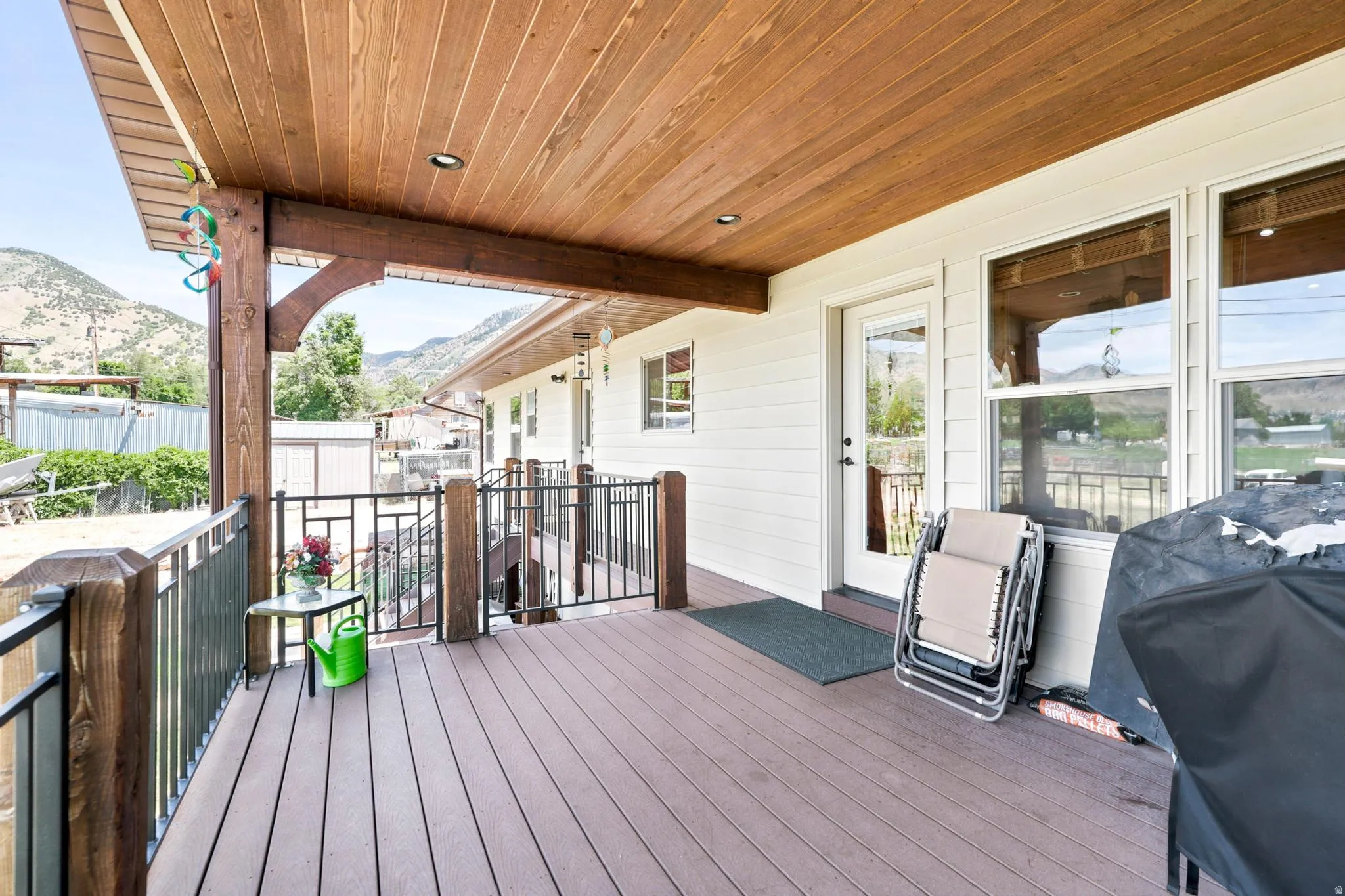 Expansive covered deck featuring wood-finish ceiling, recessed lighting, composite decking, and metal railings with wood posts