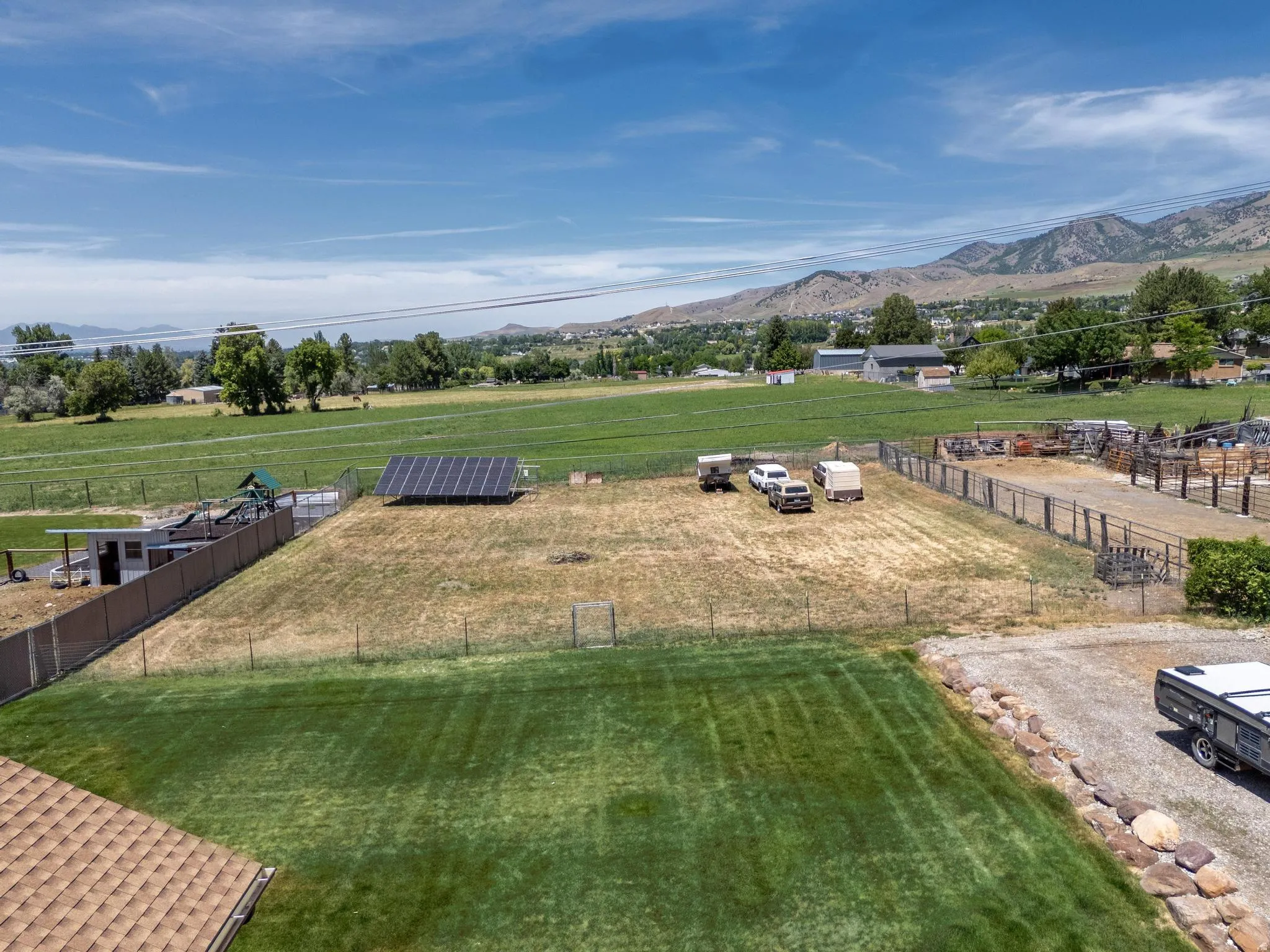 Expansive property with a large grassy area, a fenced section with solar panels, and a gravel driveway