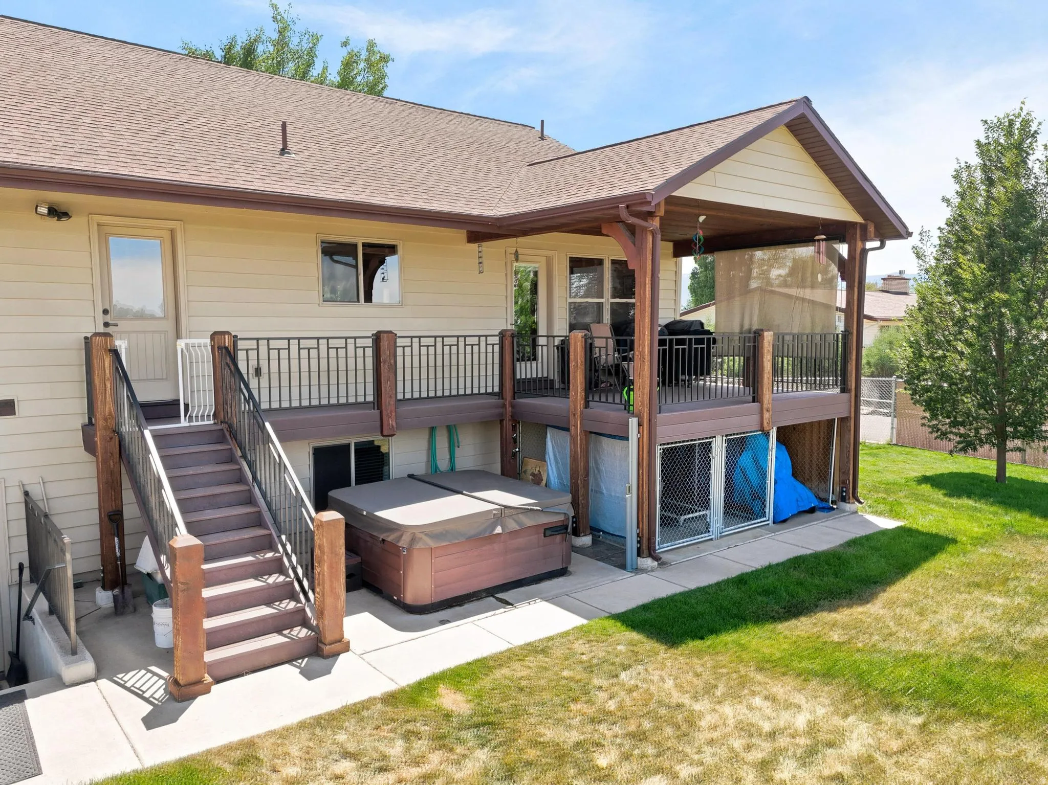Two-story exterior featuring a covered deck, lower-level patio, and hot tub