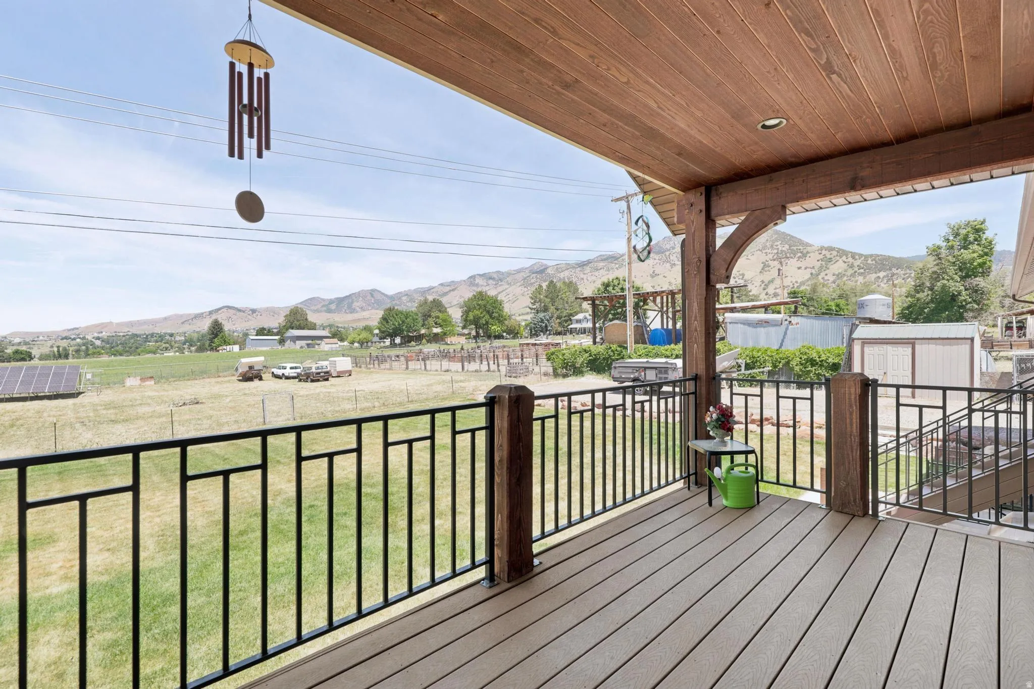 Expansive outdoor deck featuring wood-finish flooring, a wood plank ceiling, and black metal railings with geometric accents
