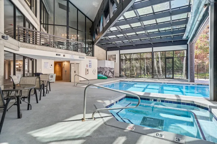 Indoor pool and hot tub area featuring a large skylight roof, extensive window walls, and access to an upper-level balcony