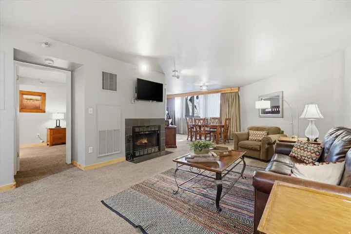 Living room featuring a fireplace with a dark tile surround, wall-mounted television, and carpet flooring