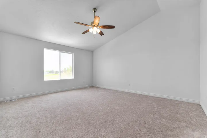 Spacious room featuring vaulted ceilings, light gray carpeting, a large window, a ceiling fan with integrated lighting, and white baseboards