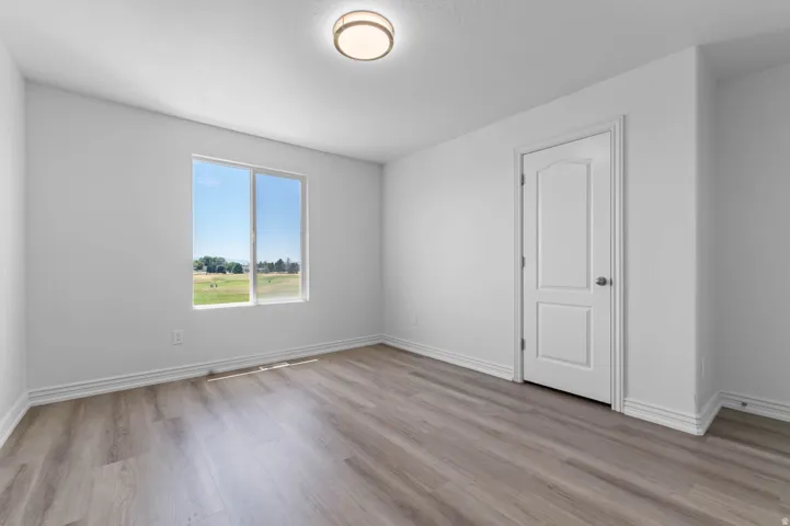 Interior room featuring wood-finish flooring, a white paneled door, and a large window