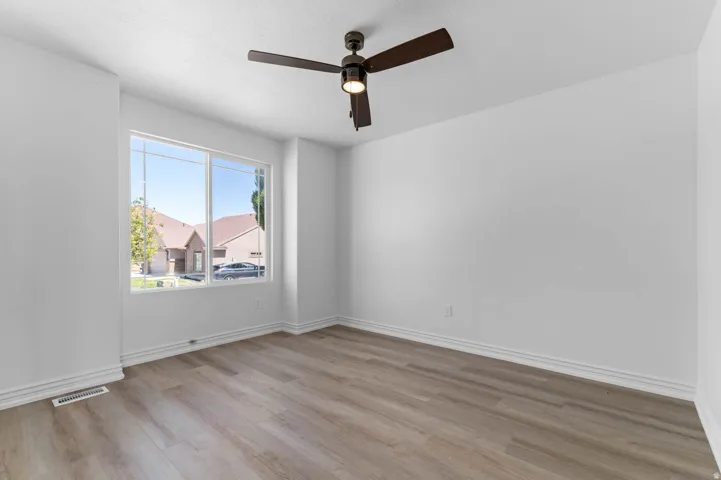 Bright room featuring a large window, a ceiling fan with integrated lighting, wood-finish flooring, white walls, and white baseboards