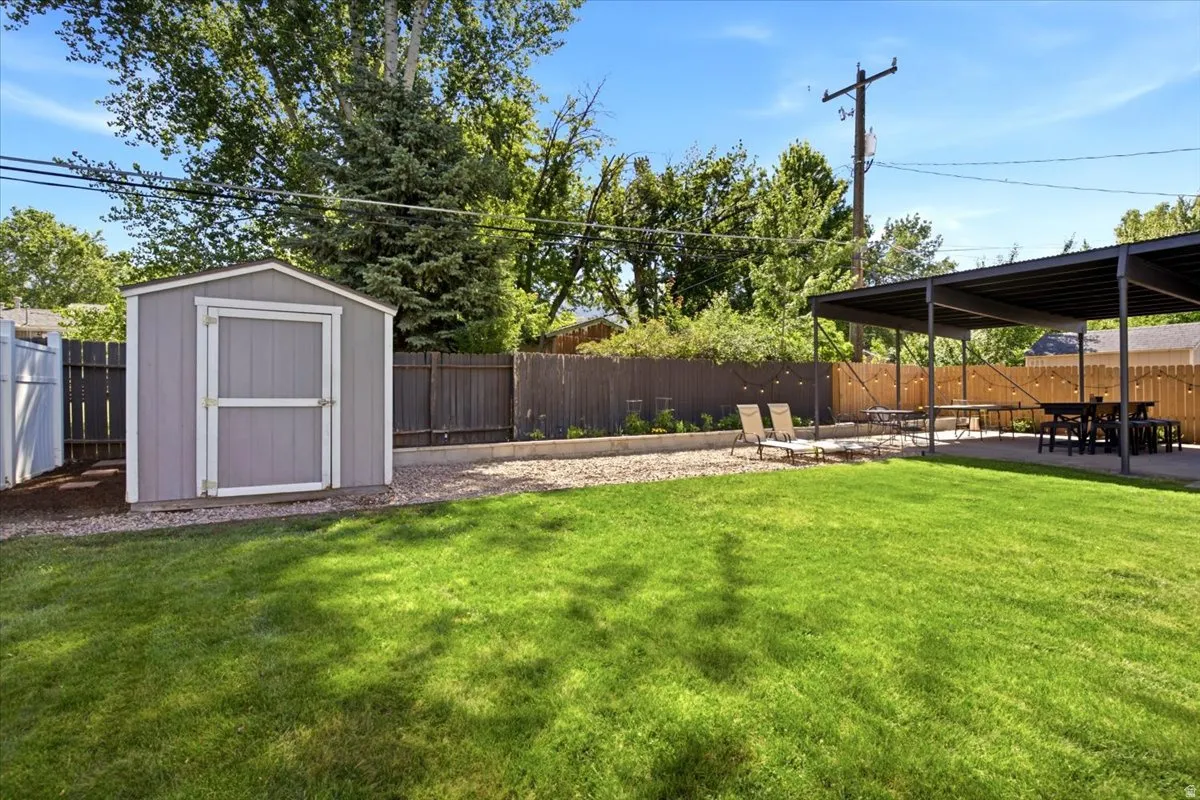 Expansive backyard featuring a lush lawn, a detached storage shed, a covered patio area, and perimeter fencing