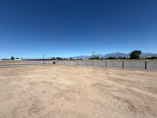 Expansive undeveloped lot featuring a stone-look perimeter wall, a clear blue sky overhead, and distant mountain scenery