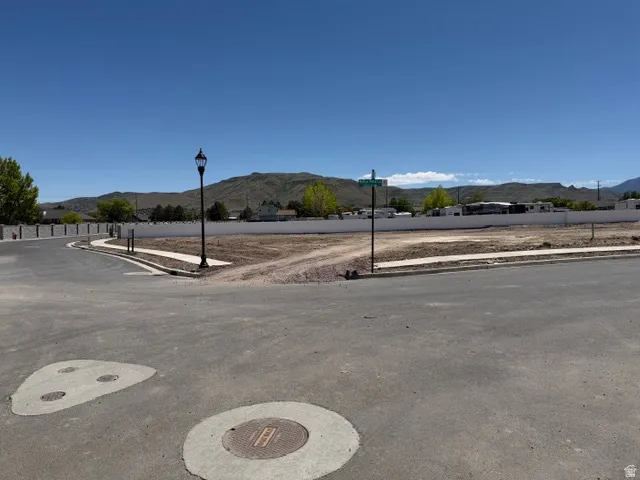 Cleared land parcel featuring paved street access, concrete sidewalks, a street lamp, and mountain scenery