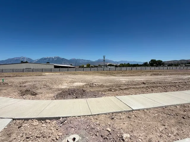 Expansive building lot featuring newly installed concrete sidewalks, a distant mountain range backdrop, and a perimeter fence