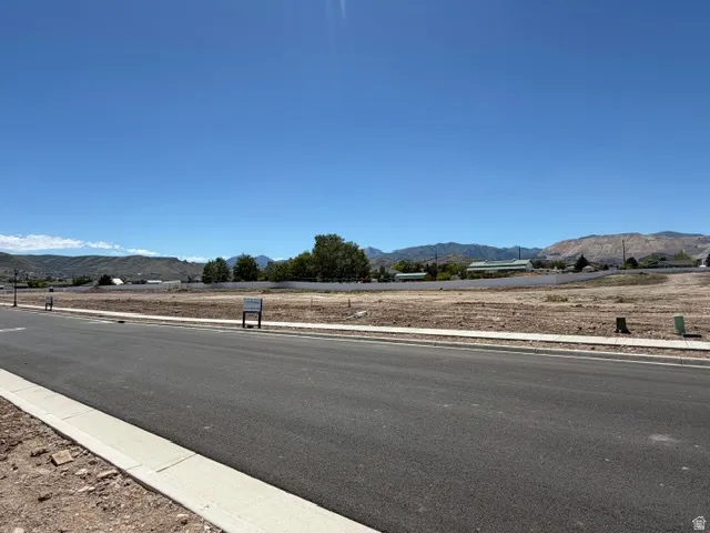 Paved road and concrete sidewalk bordering a cleared land parcel with distant mountains