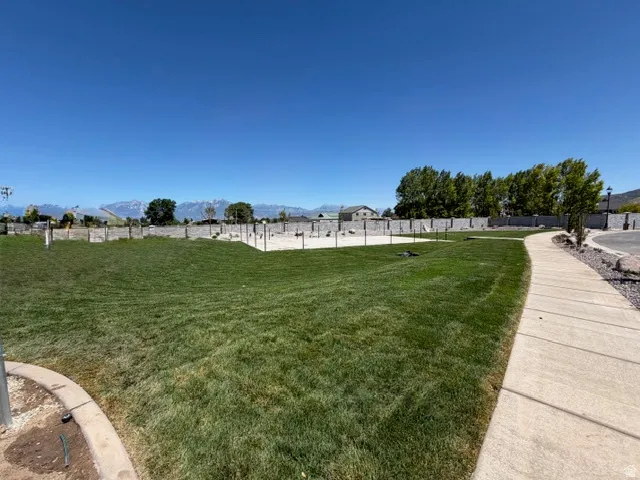 Expansive green space featuring a concrete pathway, mountain backdrop, and perimeter fencing