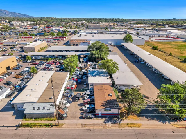 Commercial property featuring multiple buildings with flat and sloped roofs, extensive paved areas for vehicle storage, and covered parking structures