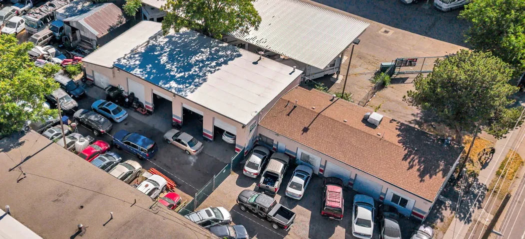 Commercial property featuring multiple service bays with roll-up doors, a large paved parking area, and a secondary building with a shingle roof