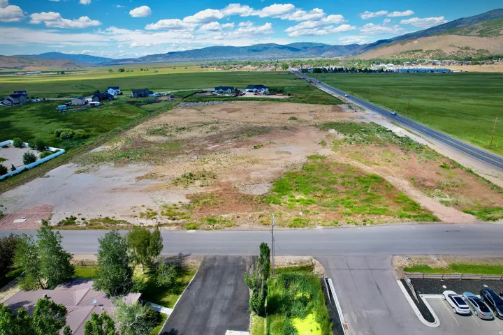 Expansive undeveloped land featuring a paved road, mountain backdrop, and scattered residential properties in the background