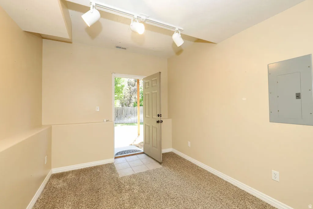 Carpeted room with track lighting, a partial dropped ceiling, and a rear exterior door with tile flooring
