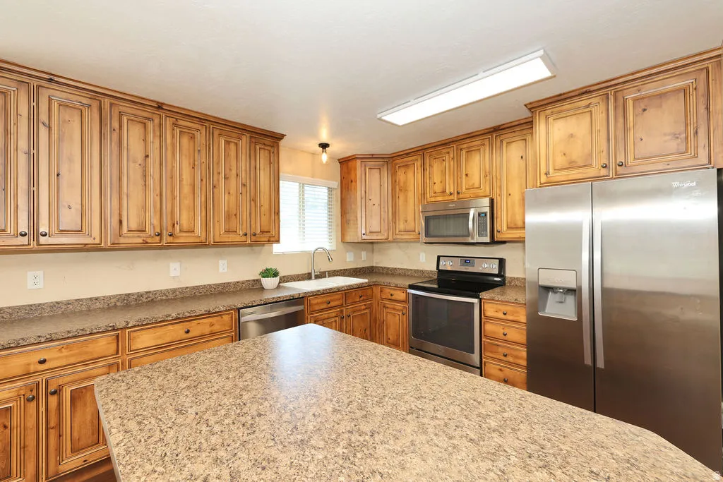 Kitchen featuring extensive wood cabinetry, granite-finish countertops, and stainless steel appliances including a refrigerator, dishwasher, and electric range