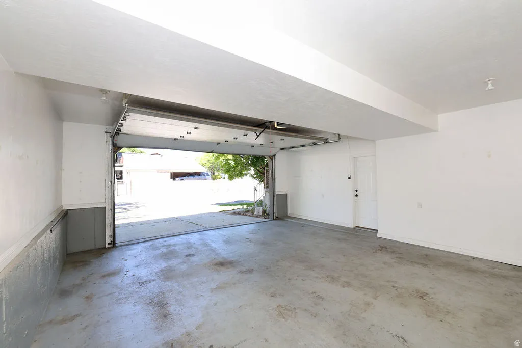 Attached two-car garage with concrete flooring, white painted walls, and a white interior door