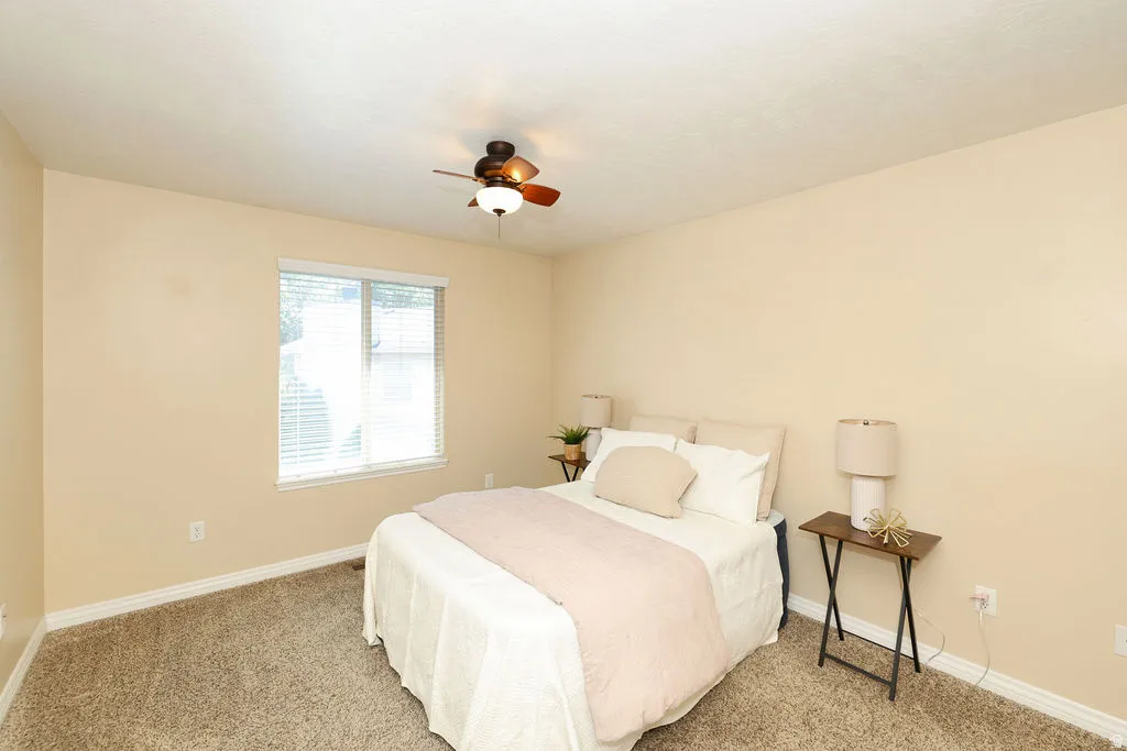 Bedroom featuring a window with blinds, a ceiling fan, neutral-toned walls, textured carpeting, and white baseboards