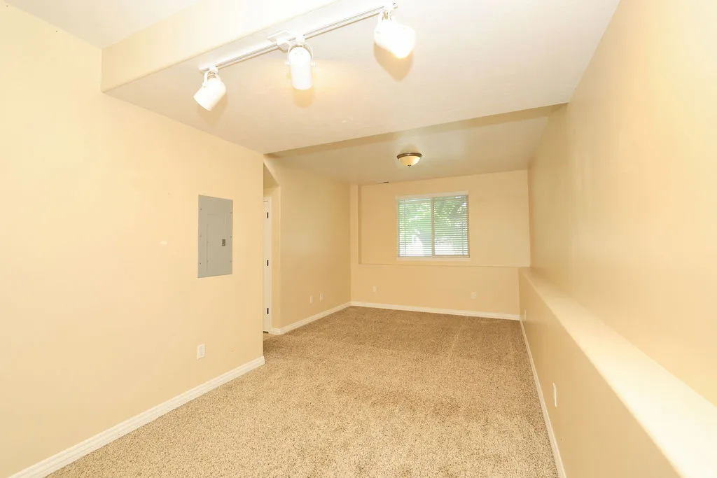 Carpeted room featuring a window with blinds, overhead lighting, and track lighting