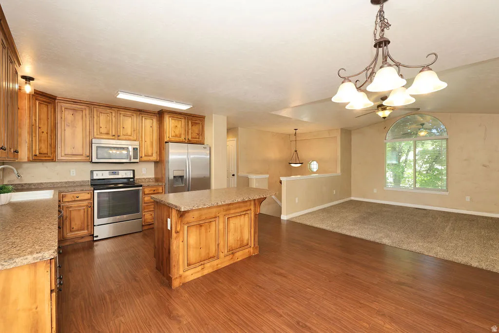 Open-concept kitchen featuring wood-finish cabinetry, stainless steel appliances, and a central island with a granite-style countertop