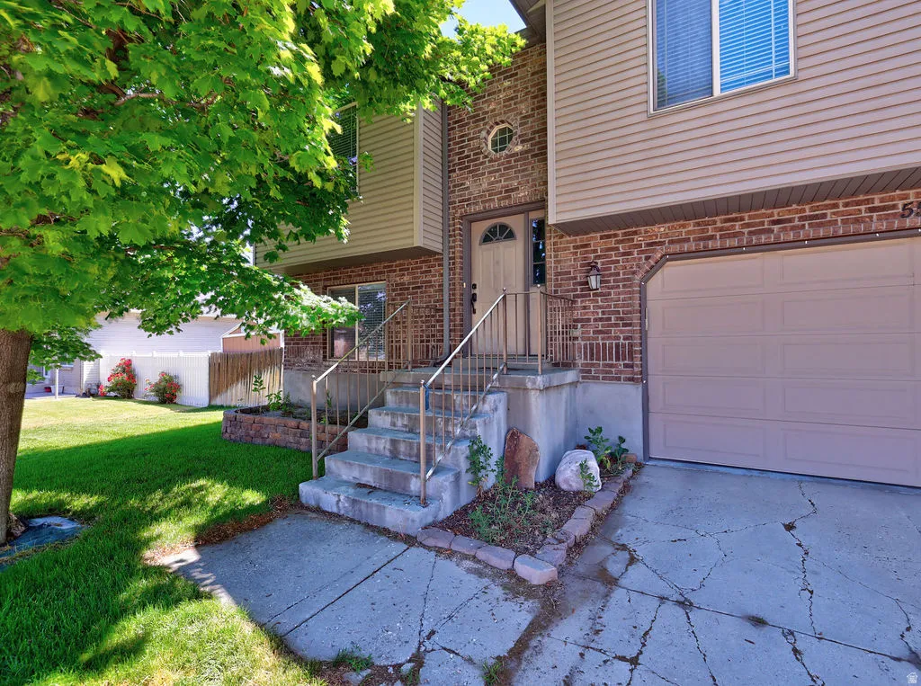 Brick and siding exterior featuring an attached garage, covered entryway, and mature landscaping