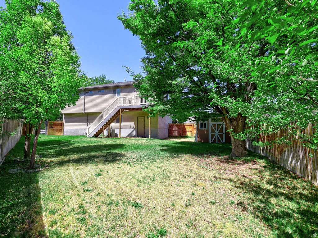 Expansive backyard featuring a multi-level deck with stairs, mature trees providing shade, a wood privacy fence, and a storage shed with white trim