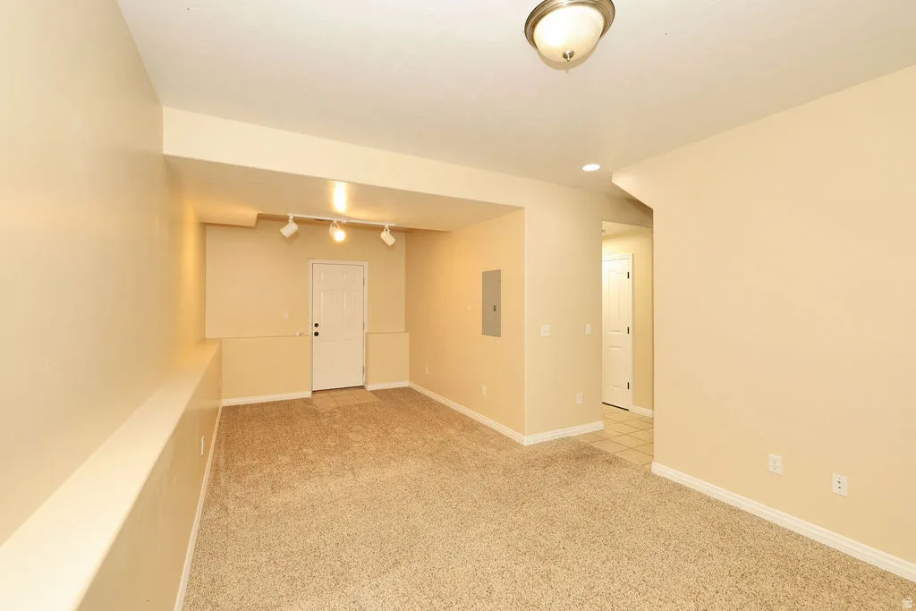 Spacious room featuring neutral carpeting, light beige wall finishes, a white paneled door, track lighting, and a flush mount ceiling fixture